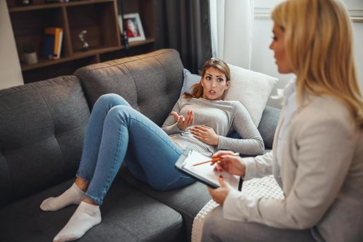 Shot of a worried young woman having a discussion with her female psychotherapist while being seated on a sofa inside of a living room.
