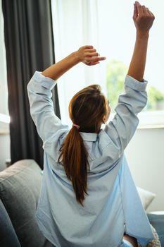 Beautiful young woman sitting on the sofa, enjoying at home.