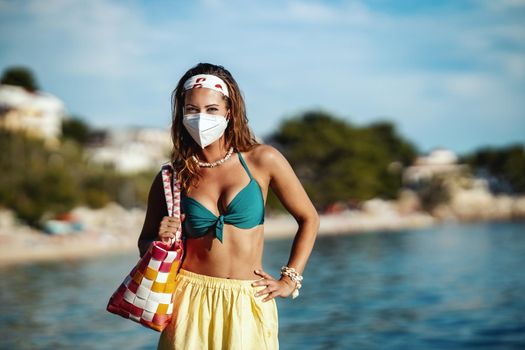 Shot of an attractive young woman in bikini with surgical mask enjoying a vacation on the beach during the COVID-19.