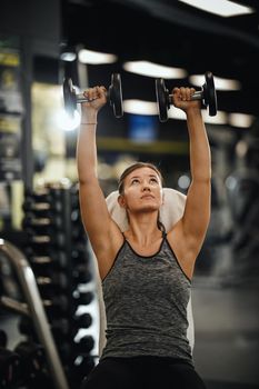 Shot of a muscular young woman in sportswear working out at the hard training in the gym. She is pumping up her shoulder muscule with heavy weight.