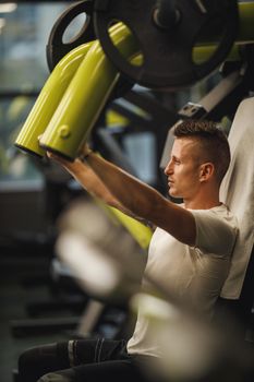 Shot of a muscular guy in sportswear working out at the cross training gym. He is pumping up chest muscule with heavy weight.