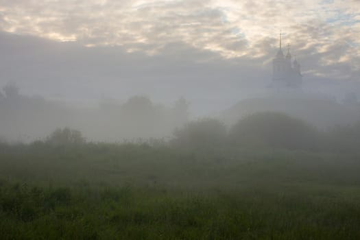 foggy summer morning landscape with the church on the hill in the background.