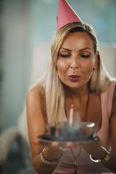 Alone attractive woman have birthday celebration at home during pandemic isolation and have video call with friends. She holding birthday cake with lighted candles.