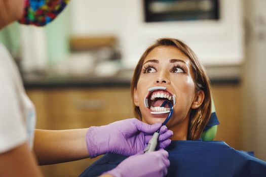 Shot of a beautiful young woman is at the dentist. She sits in the dentist's chair and the dentist preparing to sets braces on her teeth putting aesthetic self-aligning lingual locks.