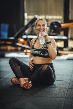 Shot of a pregnant woman drinking water and getting ready to workout at the gym.