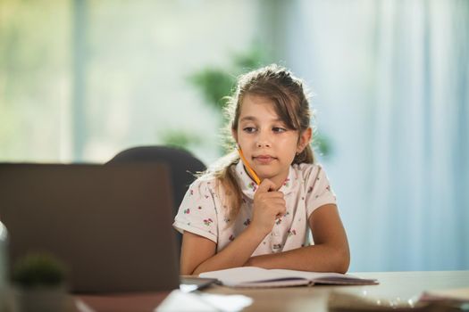 Shot of a diligent little girl using laptop to do a online lesson at home during COVID-19 pandemic.