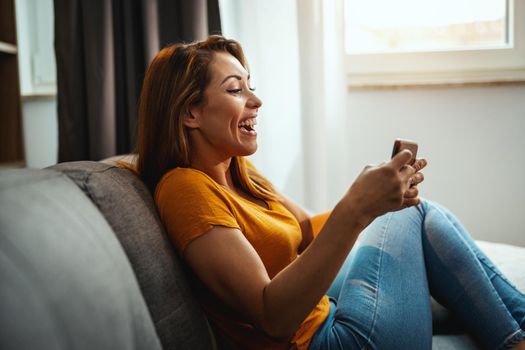 Attractive young woman sitting on the sofa and using smartphone to playing video game at home.