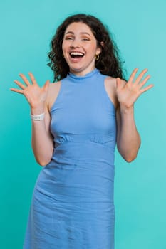Happy joyful woman shouting, raising hands in gesture I did it, celebrating success, winning, birthday, lottery jackpot goal achievemen, good news. Young girl on blue studio wall background. Vertical