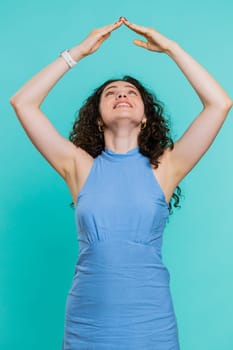 House roof about head. Young woman playing childish catching up game, feeling in safe making roof above head with hands, insurance, security service. Girl isolated on blue studio background. Vertical