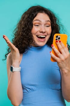Happy excited woman girl use smartphone typing browsing shouting say wow yes found out great big win, good news, lottery goal achievemen, celebrating success, winning game on blue background. Vertical