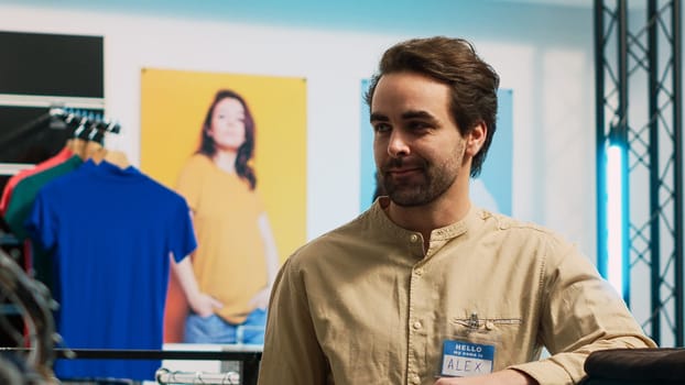 Store assistant posing in fashion department store, employee working in shopping center shop to help clients with modern clothes. Male retail worker smiling in clothing showroom.