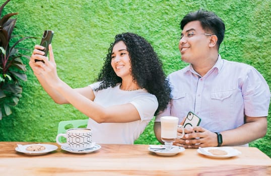 Two happy friends having a coffee and taking a selfie. Couple of friends sitting enjoying a coffee and taking a selfie