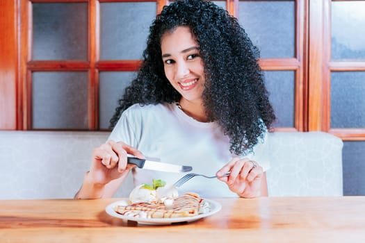 Smiling woman sitting eating chocolate crepe and ice cream. Beautiful girl eating chocolate crepe and ice cream with a fork