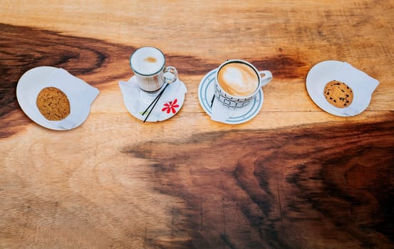 Top view of hot cappuccinos with cookie on wooden background. High angle view of cappuccinos with cookies on wooden table