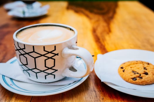 Cup of cappuccino with cookie on wooden table. Delicious hot cappuccino coffee with cookie on wooden background