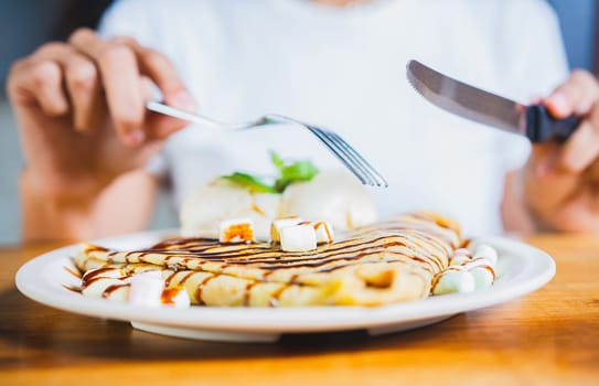 Close up of woman eating a chocolate crepe with fork. Woman hands eating chocolate crepe and ice cream with fork