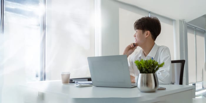 Young business man working at office with laptop and papers on desk.