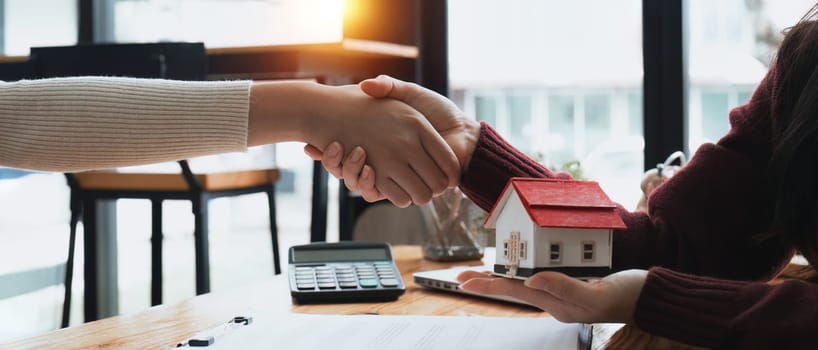 Real estate agents and customers shake hands to congratulate on signing a contract to buy a house with land.