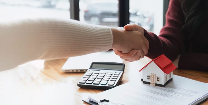 Real estate agents and customers shake hands to congratulate on signing a contract to buy a house with land.