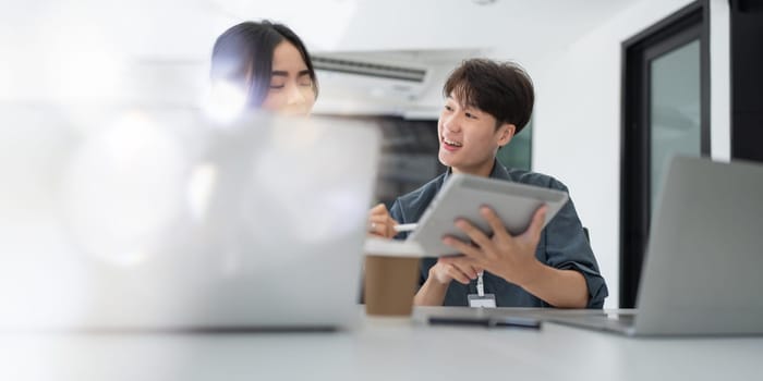 Two asian business worker looking at tablet discussing corporate strategy in teamwork, working on computer laptop in office at office.