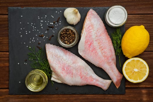Seafood. Sea perch on a black board. Red sea bass on a black board with the ingredients for it cooking. Fish on the table. Ocean perch.
