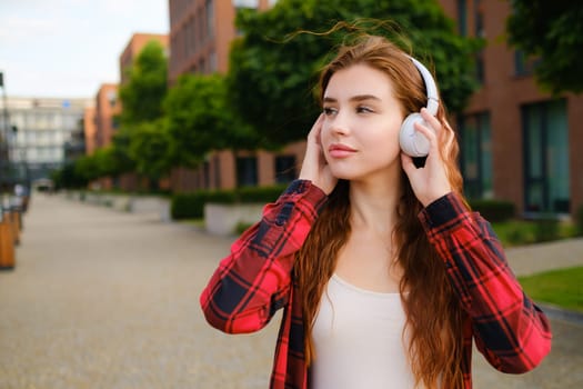 Close up portrait of a delighted young woman listening to music through wireless headphones in the modern city center