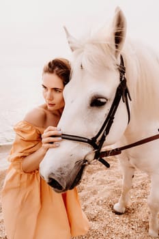 A woman in a dress stands next to a white horse on a beach, with the blue sky and sea in the background