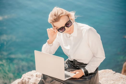 Business woman on nature in white shirt and black skirt. She works with an iPad in the open air with a beautiful view of the sea. The concept of remote work