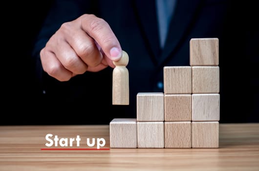 Businessman holding a wooden doll on the first step of the stairs. represents the start of a business. Startup concept. Business concept.