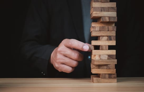 Businessman hand of businessman pulling out or placing wood block on the tower with copyspace. Business risk, strategy and planing concept idea. 