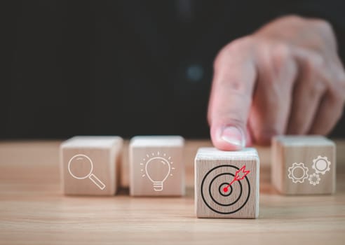 Businessman hand pushing a wooden block which prints a target icon. Business goals and objectives concept. business competition