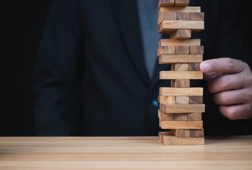 Businessman hand of businessman pulling out or placing wood block on the tower with copyspace. Business risk, strategy and planing concept idea. 