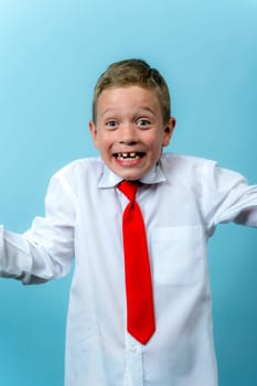 a happy funny first grader in a white shirt with a red tie is laughing. Cute Caucasian boy goes to school. Schoolboy. September 1, for the first time in the first grade. blue background, vertical photo