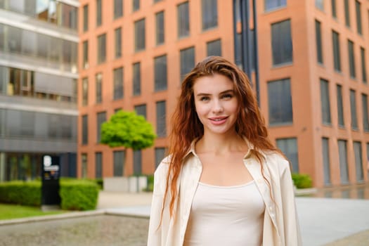 Portrait of amazing red haired woman standing in front of red stone building in the modern city center