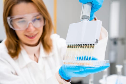 Scientist in goggles and rubber gloves uses pipette for filling 96 well plate for microbiological analysis. DNA or ELISA test.
