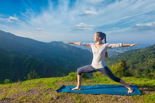 Yoga outdoors - sporty fit woman doing yoga asana Virabhadrasana 2 - Warrior pose posture outdoors in Himalayas mountains in the morning