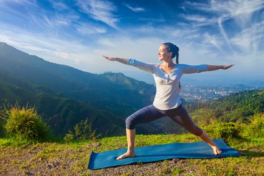 Yoga outdoors - sporty fit woman doing yoga asana Virabhadrasana 2 - Warrior pose posture outdoors in Himalayas mountains in the morning