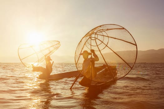 Myanmar travel attraction landmark - two traditional Burmese fishermen at Inle lake, Myanmar famous for their distinctive one legged rowing style on sunrise sunset