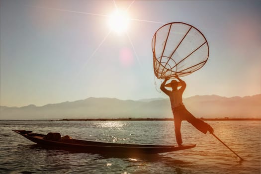 Myanmar travel attraction landmark - Traditional Burmese fisherman at Inle lake, Myanmar famous for their distinctive one legged rowing style on sunset. With light leak and lens flare