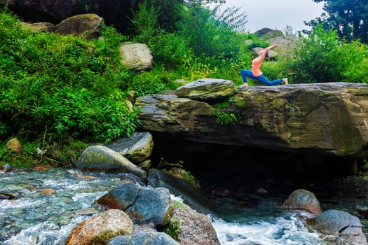 Yoga outdoors - sporty fit woman practices yoga Anjaneyasana - low crescent lunge pose outdoors in mountains