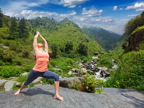 Yoga outdoors - sporty fit woman doing Ashtanga Vinyasa Yoga asana Virabhadrasana 1 Warrior pose posture at waterfall in HImalayas mountains