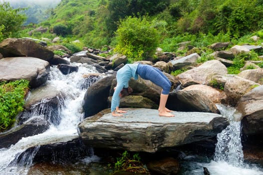 Yoga outdoors - young sporty fit woman doing Ashtanga Vinyasa Yoga asana Urdhva Dhanurasana - upward bow pose at tropical waterfall