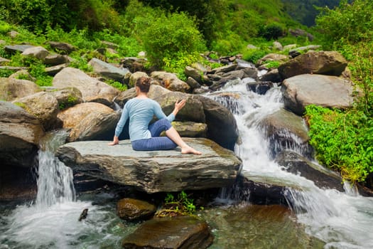 Yoga exercise outdoors - woman doing Ardha matsyendrasana asana - half spinal twist pose at tropical waterfall in Himalayas in India