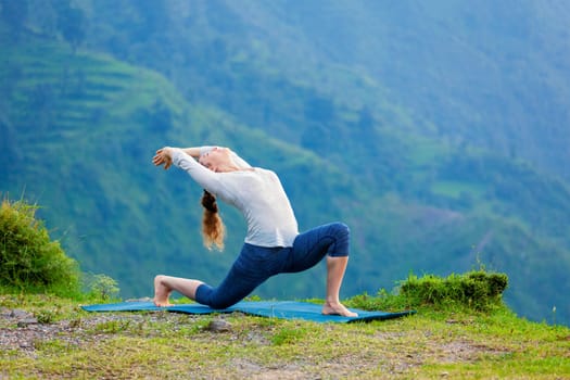 Yoga outdoors - sporty fit woman practices Hatha yoga asana Anjaneyasana - low crescent lunge pose posture outdoors in Himalayas mountains