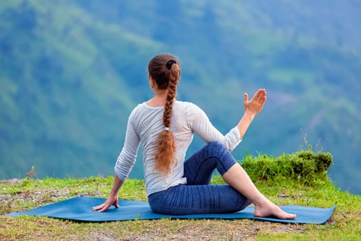 Hatha yoga outdoors - sporty fit woman doing yoga asana Parivrtta Marichyasana (or ardha matsyendrasana) - seated spinal twist outdoors in mountains
