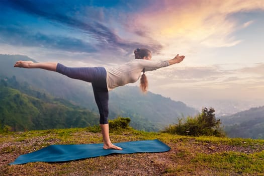 Yoga outdoors - sporty fit woman doing Ashtanga Vinyasa Yoga asana Virabhadrasana 3 Warrior pose posture in mountains