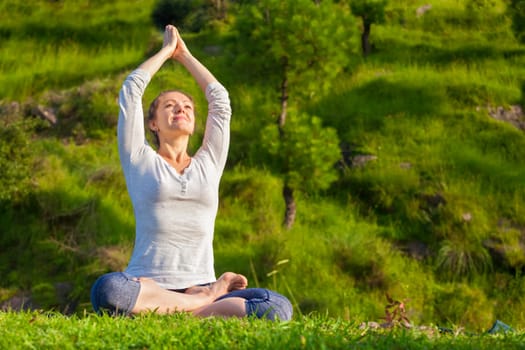 Meditation and relaxation yoga outdoors - young woman meditating and relaxing in Padmasana Lotus Pose) on green grass in forest