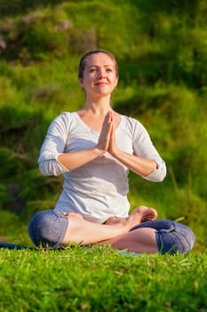 Meditation and relaxation yoga outdoors - young woman meditating and relaxing in Padmasana Lotus Pose) with chin mudra on green grass in forest