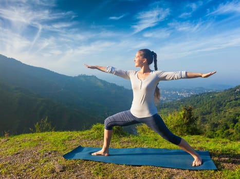 Yoga outdoors - sporty fit woman doing yoga asana Virabhadrasana 2 - Warrior pose posture outdoors in Himalayas mountains in the morning