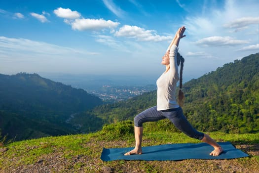 Yoga outdoors - sporty fit woman doing yoga asana Virabhadrasana 1 - Warrior pose posture outdoors in Himalayas mountains in the morning